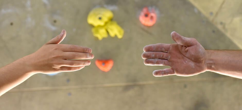 Zwei Menschen reichen sich die Hand vor Kletterwand
